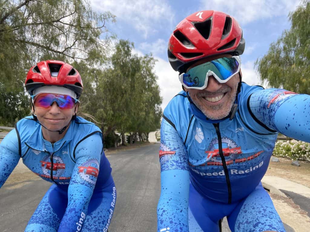 Selfie of Gil and Ofri riding bikes wearing red helmets and iSpeed Racing cycling jerseys